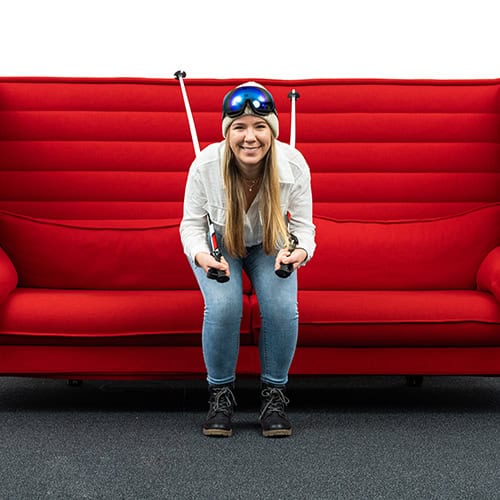 Frau mit VR-Brille und Joysticks auf rotem Sofa.